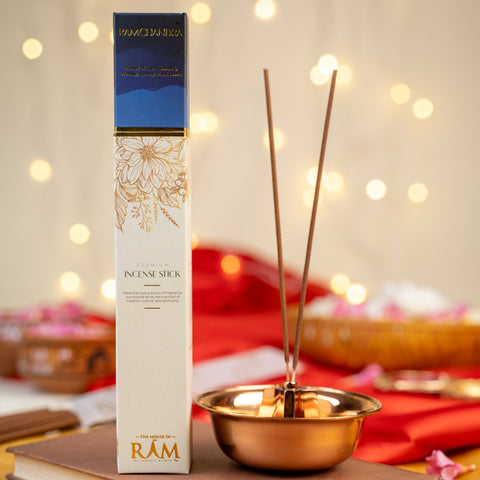 Premium incense stick packaging labeled "ramchandra" with notes of sandalwood and oud, placed beside a copper incense holder with two incense sticks Premium incense stick packaging labeled "ramchandra" with notes of sandalwood and oud, placed beside a copper incense holder with two incense sticks