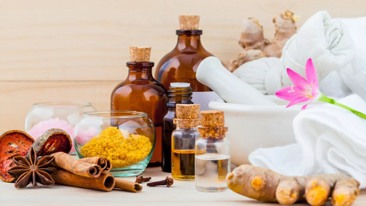 A collection of herbal ingredients, oils, and spices, featuring amber bottles, colorful powders, and a flower, arranged on a wooden surface.