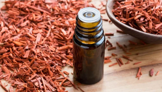 A small amber glass bottle of sandalwood essential oil placed on a wooden surface, surrounded by sandalwood chips.