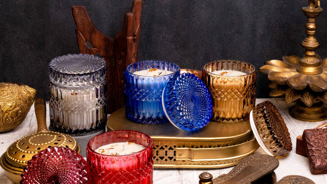 A collection of colorful scented candles in decorative jars, surrounded by ornate metal trinkets and a candle holder on a rustic surface.