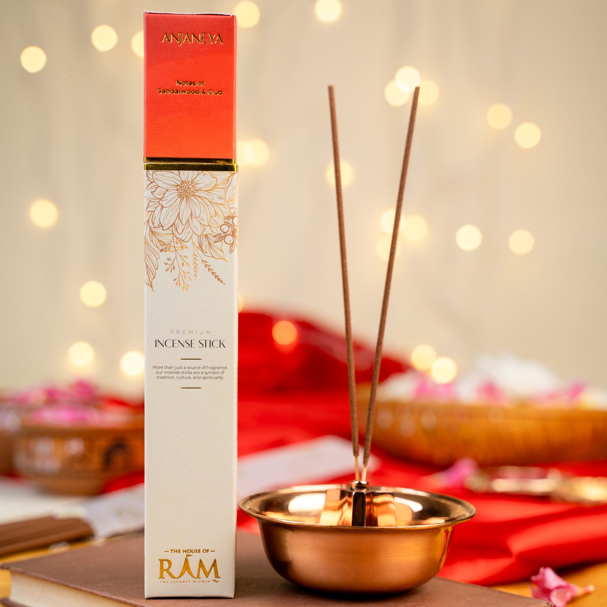 Premium incense stick packaging labeled "Anjaneya" with notes of sandalwood and oud, placed beside a copper incense holder with two incense sticks