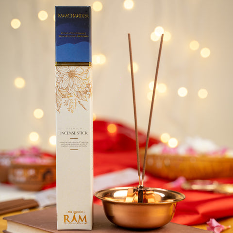 Premium incense stick packaging labeled "ramchandra" with notes of sandalwood and oud, placed beside a copper incense holder with two incense sticks